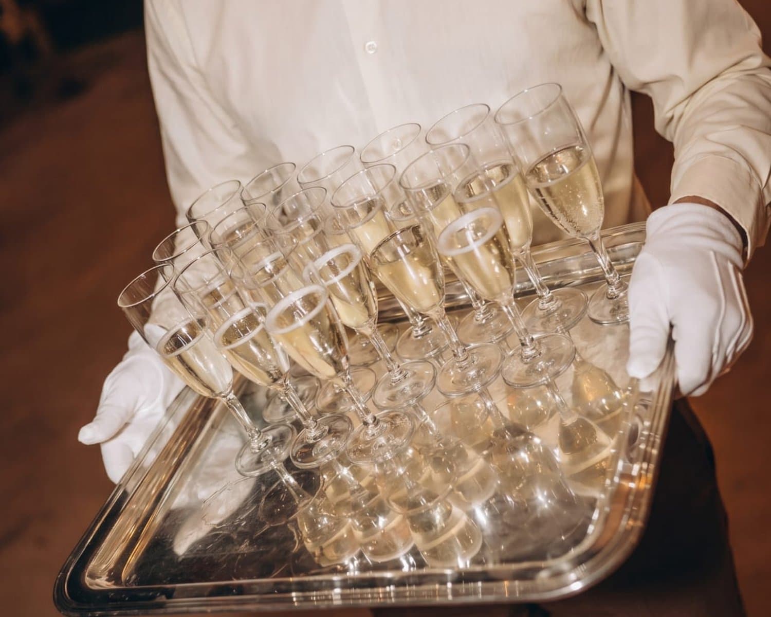 A server carrying a silver tray of filled champagne flutes