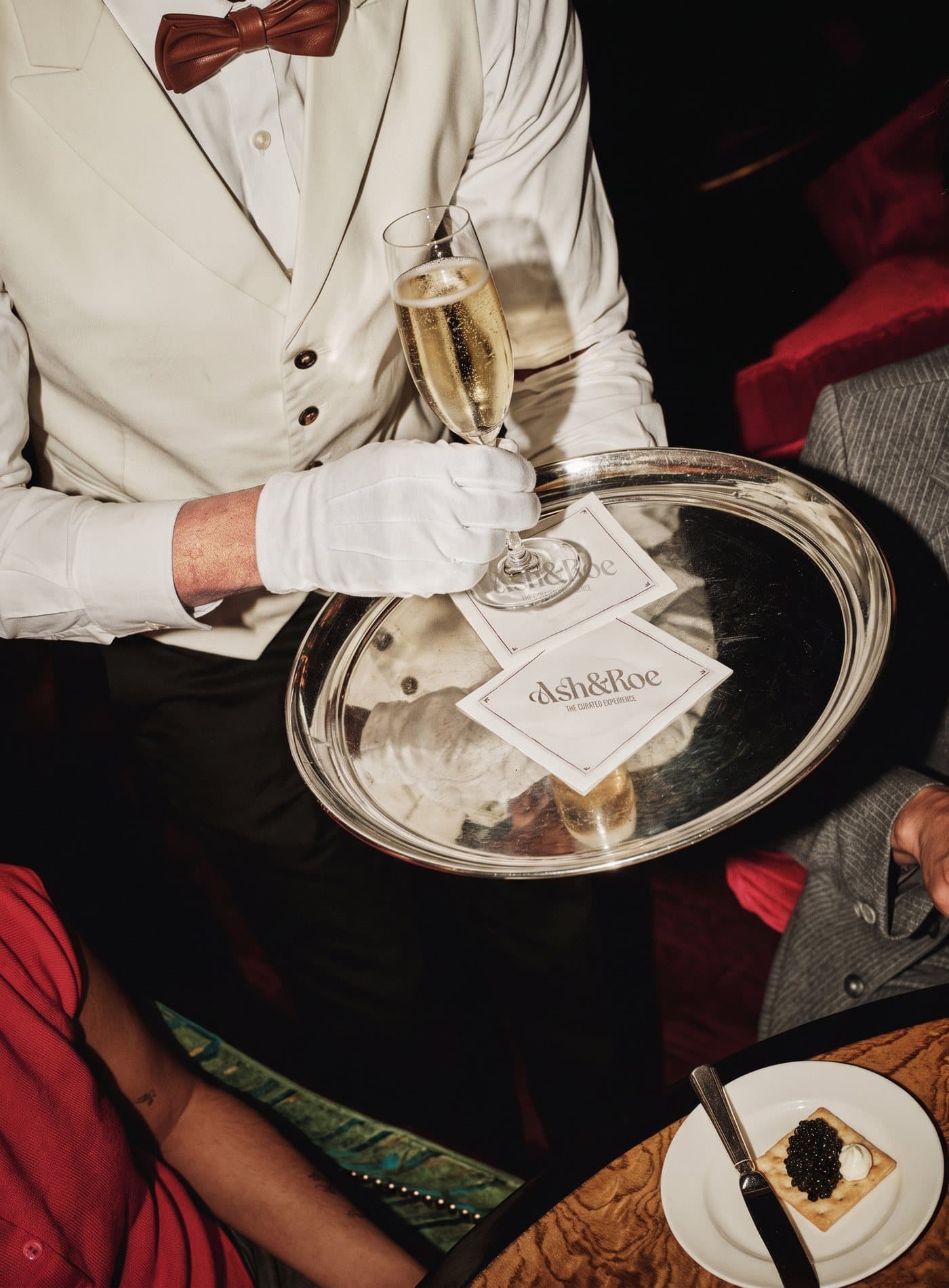 A server in a white dinner jacket carrying a silver tray of champagne