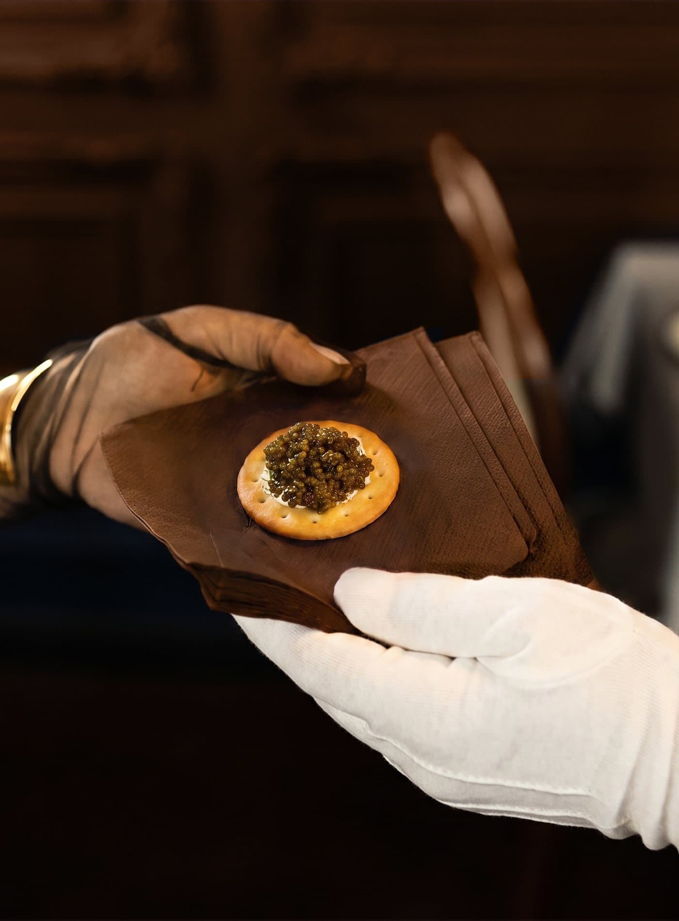 A white-gloved hand presenting caviar on a wooden board