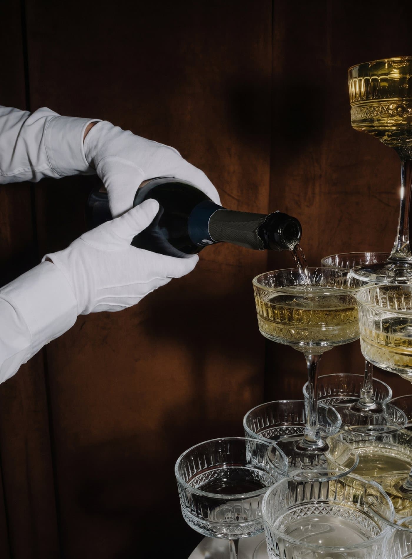 White-gloved hands pouring champagne into a tower of coupes