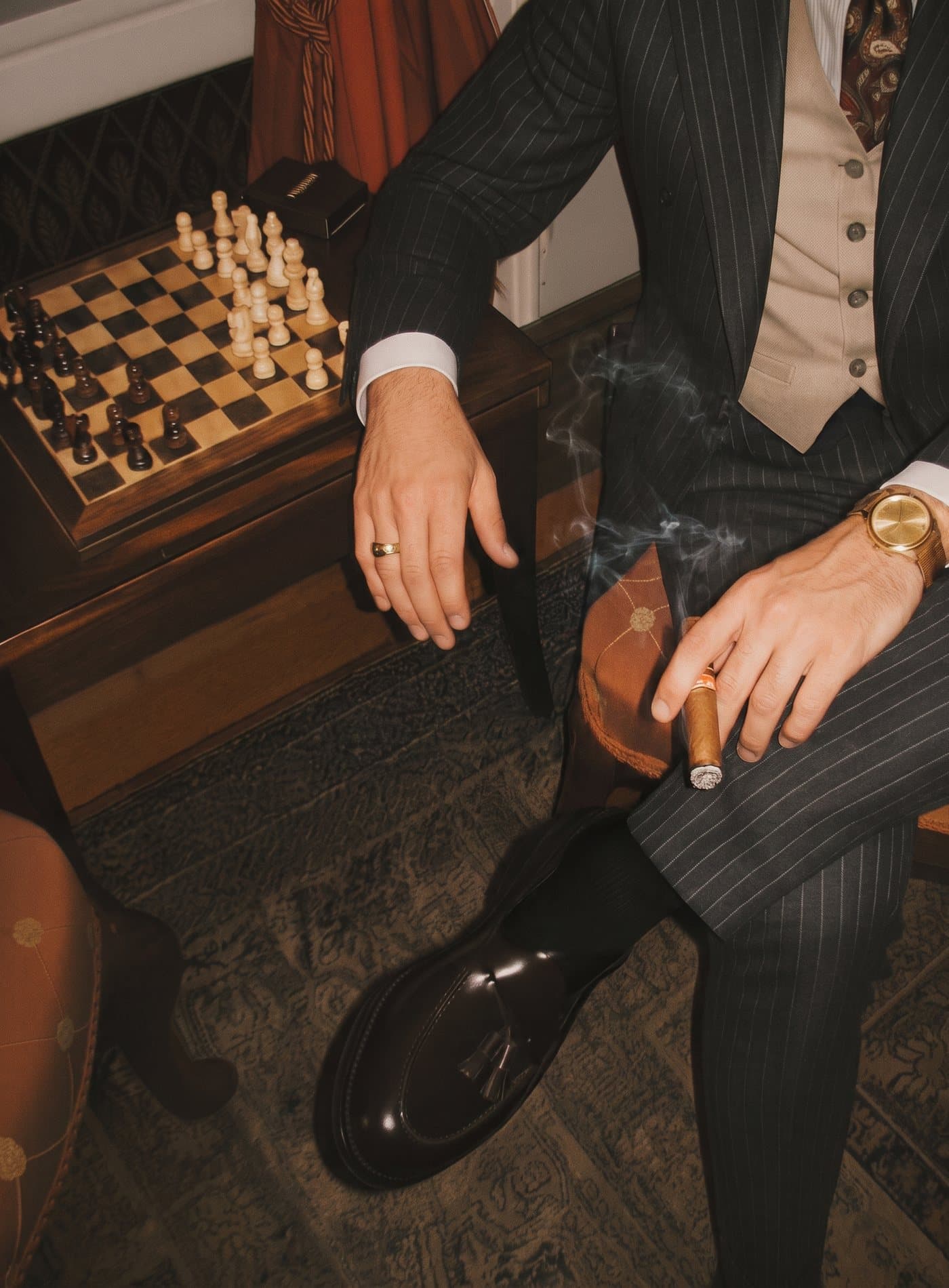 A guest in a pinstripe suit with a lit cigar beside a chessboard